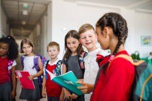 A group of cheerful small school kids with bags in corridor, talking