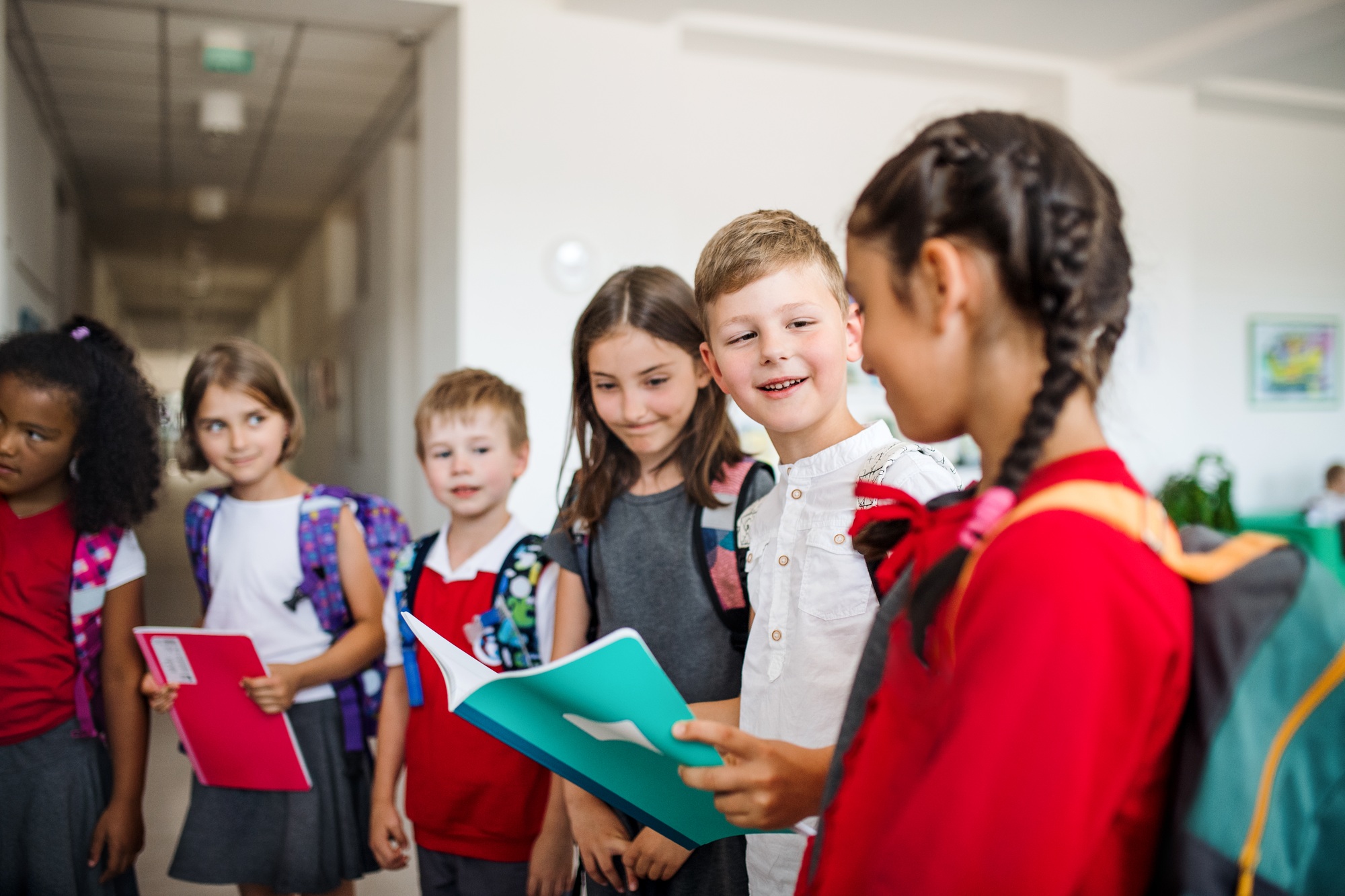 A group of cheerful small school kids with bags in corridor, talking