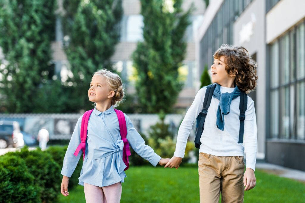 adorable excited schoolkids with backpacks holding hands and looking up