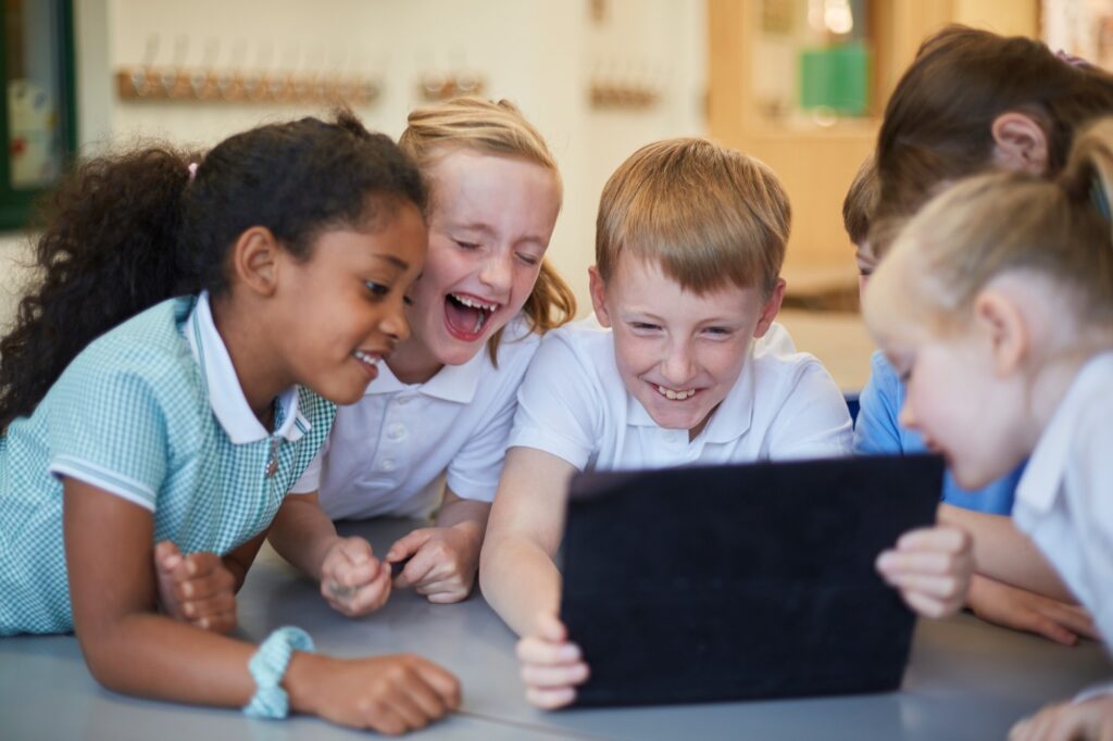 Schoolboys and girls laughing at digital tablet in classroom at primary school